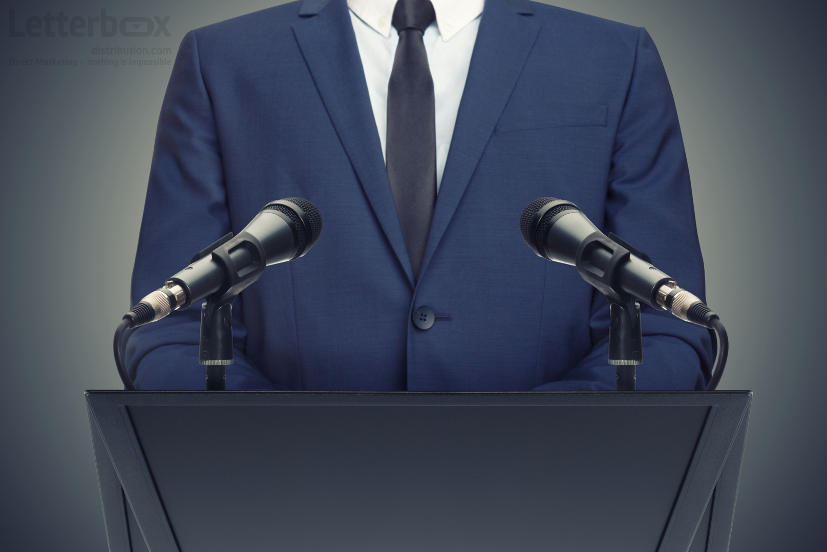 a politician is standing at a podium with two microphones on it. He is wearing a blue suit and a black tie