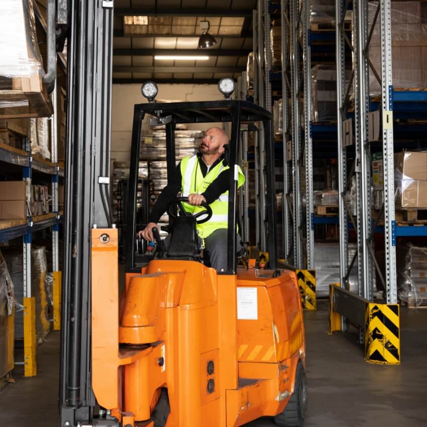 a man is sat in a forklift and is expertly driving it around a warehouse