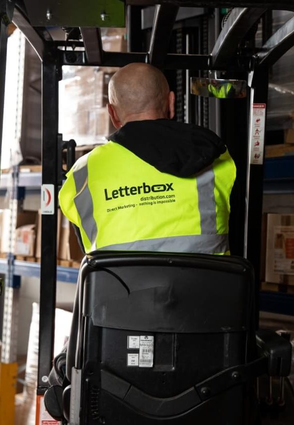 a man sits upon a forklift whilst wearing a yellow high-vis jacket. He is facing away from the camera so can only see his back