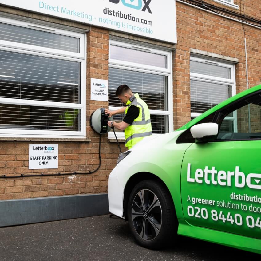 a man is plugging in an electric car to be charged. The car is Letterbox branded and is green and white
